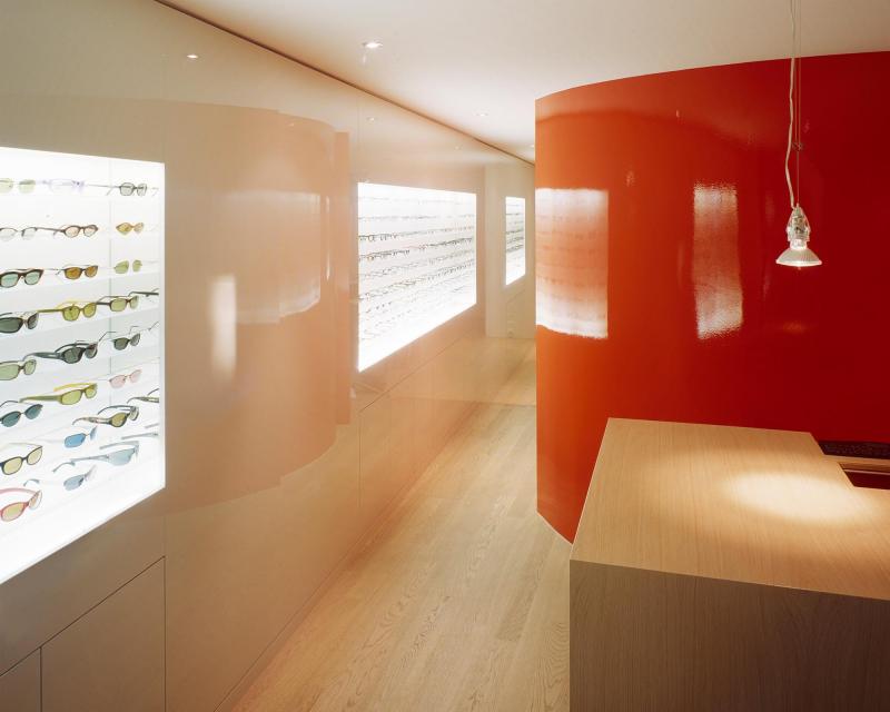 Optik Viegener Verkaufskorpus in Eiche und Brillenwand in Schleiflack vor orangefarbenem Treppenhaus 