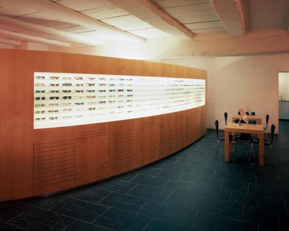 Dudli Optik Verkaufsraum mit geschwungener Brillenwand und Beratungstische 