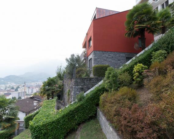 Umbau Ferienhaus Casa Sogno mio Locarno in oxidrot KEIM Farbe gestrichen und mit neuer Gaube auf Steinsockel von Palmen umgeben 