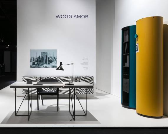 IMM Cologne 2017 Wogg Amor collection Stripe Moderato desk and chair in front of white wall with picture of Trix and Robert Haussmann