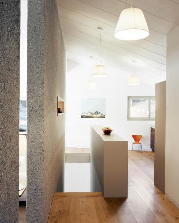 Holiday Home Celerina wall element made of bush-hammered concrete along the stair and view to the kitchen 