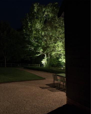 Conversion of barn at Chapel House Farm, Oakwood Hill View into the garden with illuminated oak trees and path 