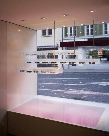 Urech Optik optician store detail glass display cabinet and backlighted floor from the display window