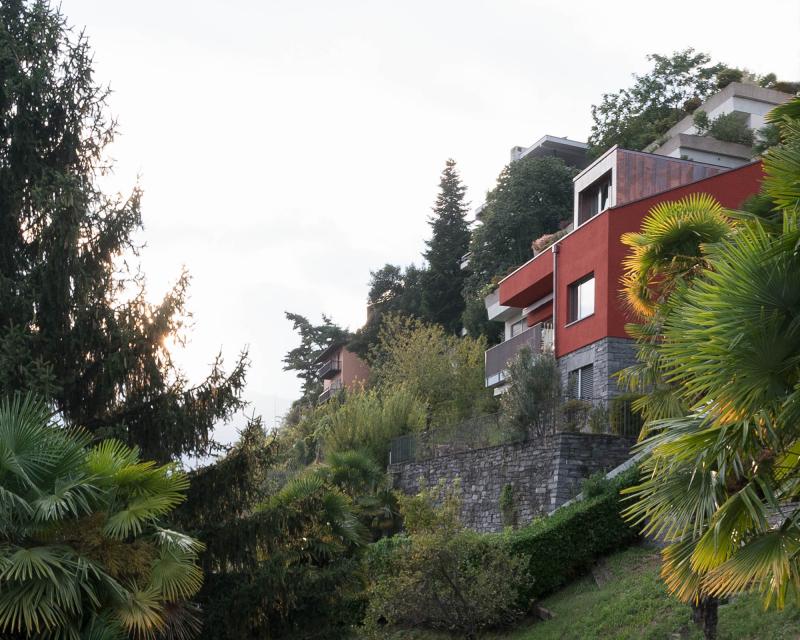 Umbau Ferienhaus Casa Sogno mio Locarno in oxidrot KEIM Farbe gestrichen und mit neuer Gaube auf Steinsockel von Palmen umgeben 