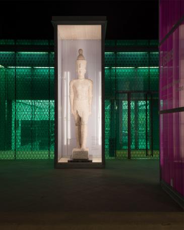 Osiris exhibition Museum Rietberg Enclosures in hot-dip galvanised steel and polycarbonate panels in violet, colossal statue of the king in front of the emerald building by night