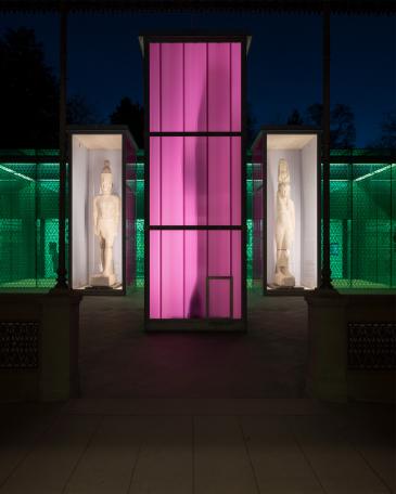 Osiris Ausstellung Museum Rietberg drei Einhausungen in feuerverzinktem Stahl und Polycarbonatplatten in viola Farbton wie Laternen leuchtend vor dem Smaragdbau bei Nacht 